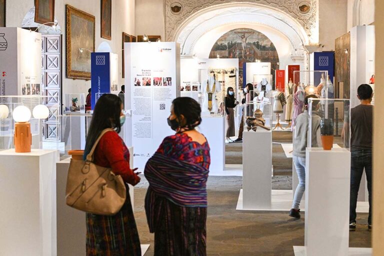 Dos mujeres platican dentro de una exposición en un recinto colonial